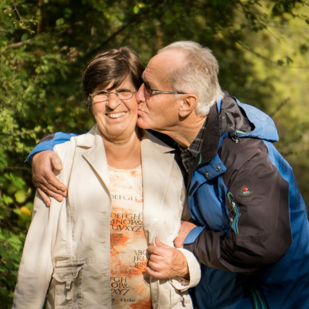 old man in retirement kissing his wife on the cheek in the park